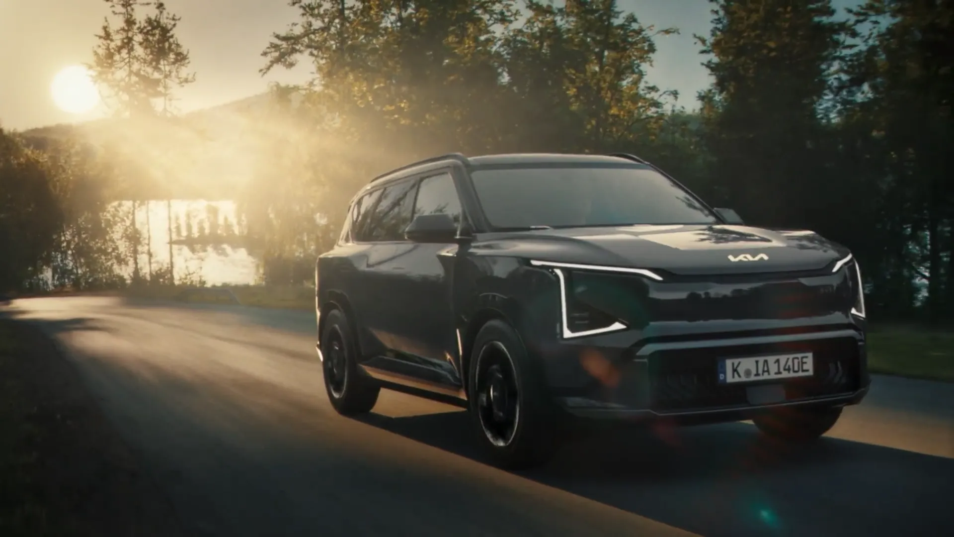 Tmavá Kia EV5 na silnici v protisvětle u jezera