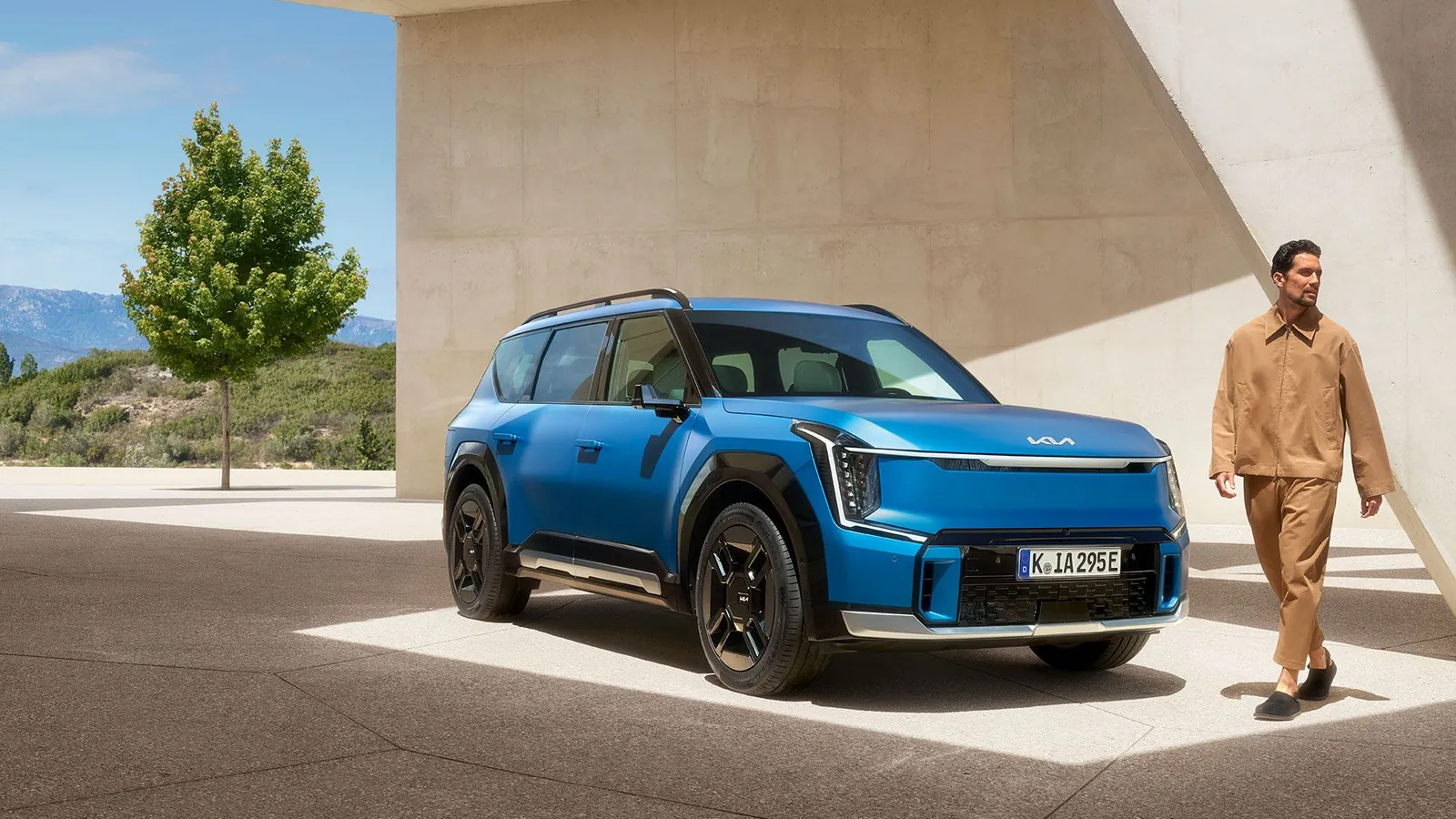 Modrá Kia EV9 a muž pod betonovou stříškou